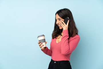 Young mixed race woman isolated on blue background holding coffee to take away and a mobile