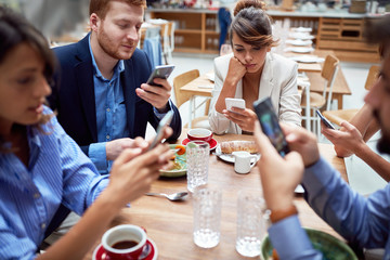 group of young caucasian people having unsocial lunch in restaurant, using their cell phones and not talking to each other. technology, social issues - obrazy, fototapety, plakaty