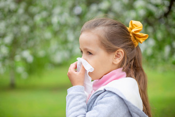 Allergy.Little girl is blowing her nose near spring tree in bloom.