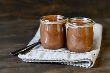 Chocolate mousse in small jars on a wooden background and a gray napkin. Selective focus.