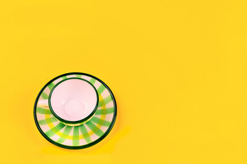 Beautiful little green striped tea coffee cup and saucer on a yellow background. The concept of home tea drinking, comfort.