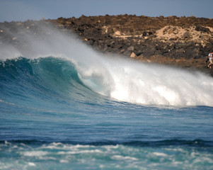 eine Welle bricht vor einer steinigen Küste und wirft eine röhre