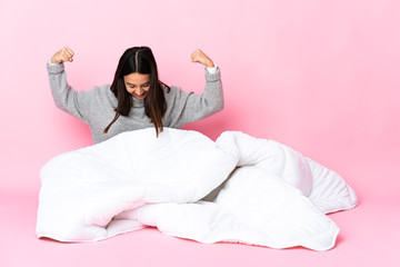 Young mixed race woman wearing pijama sitting on the floor doing strong gesture