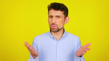 Emotional bearded man in a light blue shirt says no and shakes his hands in front of him on a yellow background with copy space. Place for text or product. 4K footage