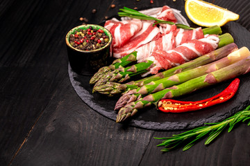 asparagus wrapped in fatty bacon, ham on a slate board. top view. Food recipe background