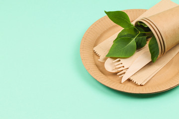 Wooden and paper utensils on a green background. Ecological disposable tableware.