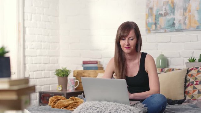 Casual woman sitting on bed working online from home with laptop computer. Stay at home and work in home office.