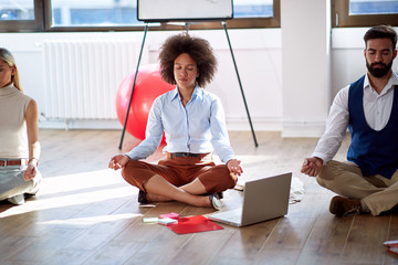 Coworkers practicing meditation at work. Coworkers sitting on the floor with computer and work...