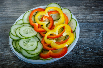 closeup sliced cucumber, red and yellow pepper served in white plastic plate