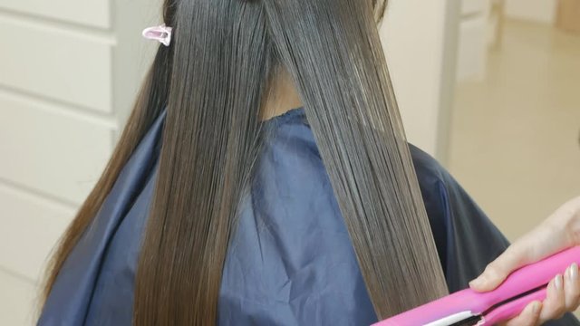 Hair straightening with keratin. The hairdresser aligns the woman's hair with a special pink hair straightener. Hair Shine. 4K