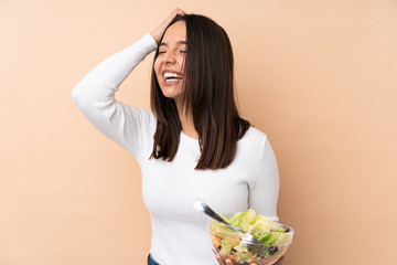 Young brunette girl holding a salad over isolated background smiling a lot