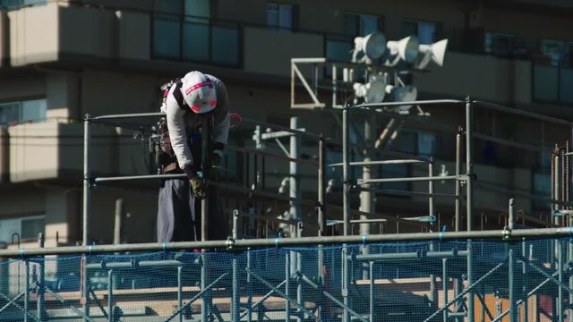 Construction worker on a building site in Japan. He is working with a spanner on scaffolding and is wearing a hard hat