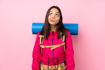 Young mountaineer girl with a big backpack over isolated pink background and looking up