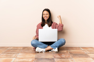 Young mixed race woman with a laptop sitting on the floor celebrating a victory