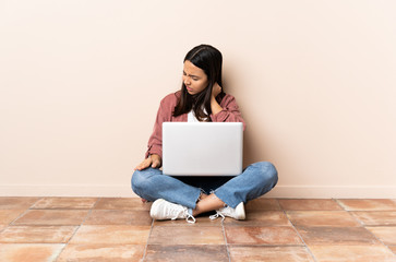 Young mixed race woman with a laptop sitting on the floor with neckache