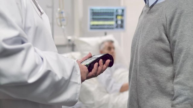 paying hospital medical bill,doctor using credit card reader machine to pay patient treatment while he's lying on bed
