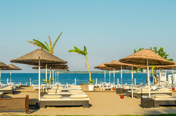 Empty sandy beach at hotel without tourists. Loose white plastic sunbeds. calm blue sea. Summer holiday on coast concept. Vacation background. Holiday backdrop.