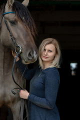 Beautiful young girl next to a horse in the stable against a dark background.