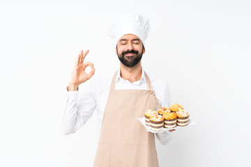 Young man holding muffin cake over isolated white background in zen pose