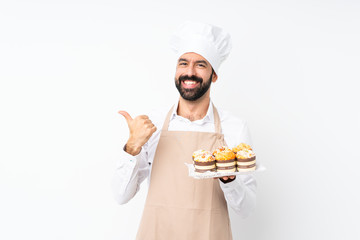 Young man holding muffin cake over isolated white background with thumbs up gesture and smiling