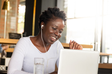 Young African woman with earphones, smiling and looking at laptop