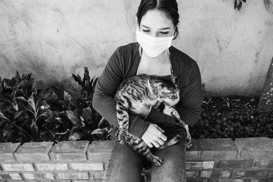 Portrait of a cute house cat lying with her owner at home. A young girl in a medical mask petting a kitten. Black and white edition - Concept of love and animal mascot