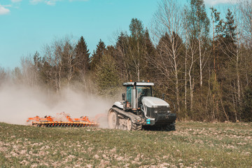 In the spring, a farmer pulls harrows with a modern tractor and sows a field with beets. Sowing...