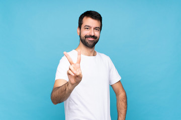 Young man with beard  over isolated blue background smiling and showing victory sign