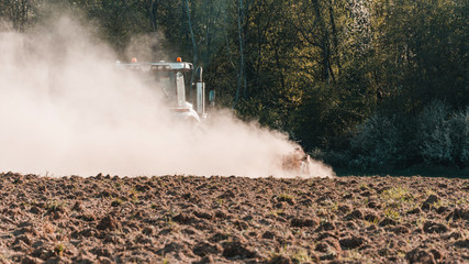 Fototapeta premium In the spring, a farmer pulls harrows with a modern tractor and sows a field with beets. Sowing campaign on agricultural land during tillage.