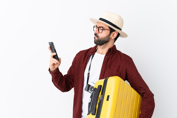 Traveler man man with beard holding a suitcase over isolated white background thinking and sending a message