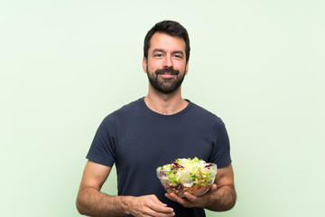 Young handsome man with salad over isolated green wall keeping the arms crossed in frontal position