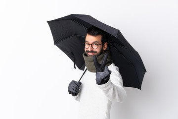 Caucasian handsome man with beard holding an umbrella over isolated white wall smiling and showing victory sign