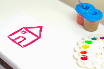 Children's creativity. Children's drawing of simple red house by watercolors on white sheet of paper.