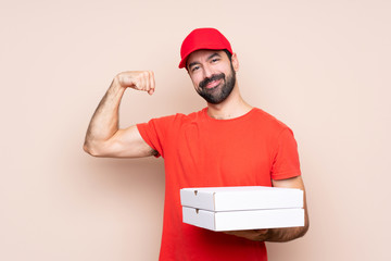 Young man holding a pizza over isolated background doing strong gesture