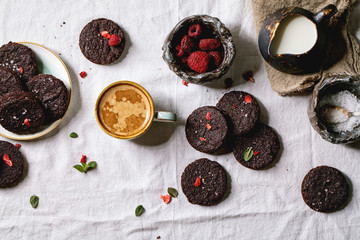 Homemade dark chocolate salted brownies cookies decorated by dried and fresh raspberries, with salt flakes, berries, mint, milk and cup of coffee over white cotton cloth. Flat lay, space