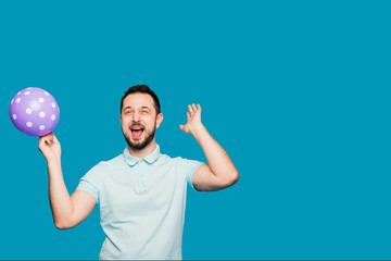 A handsome man holds a balloon in his hand and rejoices and screams at a holiday or birthday. A man...