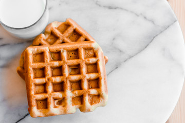 Fresh sweet Belgian or viennese waffles and a glass of milk on white marble background. Close up. Top view. Space for text