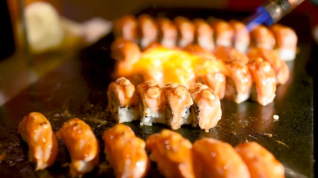 A chef is cooking sushi on a grill. The chef is using a flame to cook the sushi. The sushi is made with rice, fish, and vegetables. The sushi is arranged on a plate and is ready to be served.