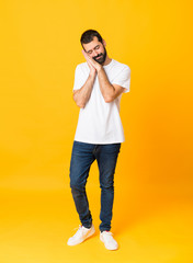 Fototapeta na wymiar Full-length shot of man with beard over isolated yellow background making sleep gesture in dorable expression