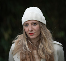 Blonde woman with white wool beanie and trench coat in a park