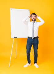 Full-length shot of businessman giving a presentation on white board over isolated yellow background frustrated and takes hands on head