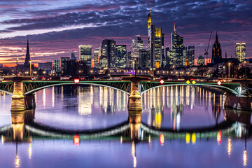 Fototapeta premium Frankfurt City Skyline and River Bridge at Night Featuring Illuminated Skyscrapers and Calm Evening Atmosphere