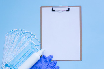 Medical mask, gloves and hand sanitizer for protecting from infection and blank clipboard with blank paper on blue background. Mock up. Top view. Flat lay. Copy space. 