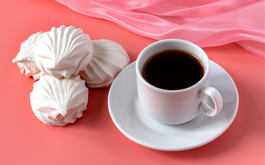 a cup of strong aromatic coffee and and a delicate white vanilla marshmallow on a pink background. place for text