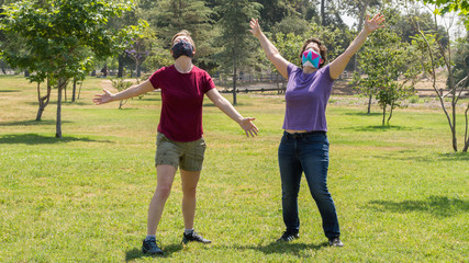 two Caucasian women wearing face masks celebrating their freedom from quarantine outdoors at a park on a sunny day