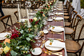 in backyard of villa in Tuscany there is banquet wooden table decorated with cotton and eucalyptus compositions, glasses, candles and plates are placed on table