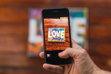 Homosexual woman photographs with her phone a watercolor that she has painted with the word Love.
