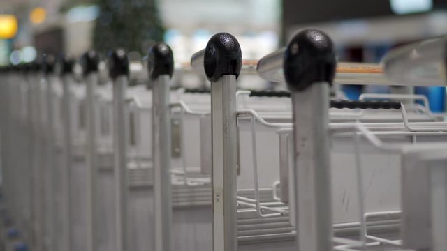 Row of empty luggage carts at airport terminal, airport baggage trolley parking lot, tall illuminated Christmas tree inside of international terminal.