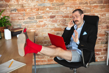 Greeting. Young man without pants but in jacket working on a computer, laptop. Remote office during...