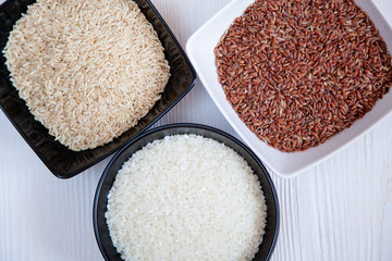 Different types of rice in cups on the table. White, brown and red.